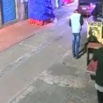 Cena de rua com pessoas, calçada e fachada de loja. Um homem caminha na calçada.