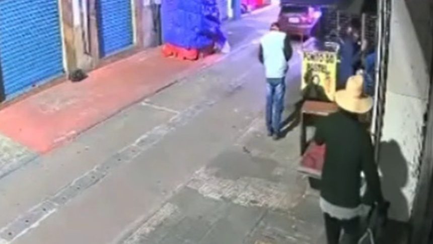 Cena de rua com pessoas, calçada e fachada de loja. Um homem caminha na calçada.