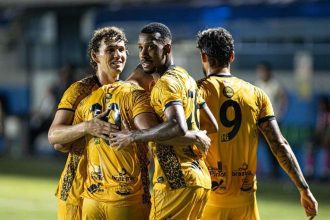 Jogadores do Amazonas FC celebrando um gol, abraçados e vestindo uniformes amarelos.