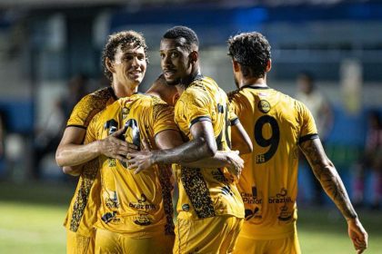 Jogadores do Amazonas FC celebrando um gol, abraçados e vestindo uniformes amarelos.