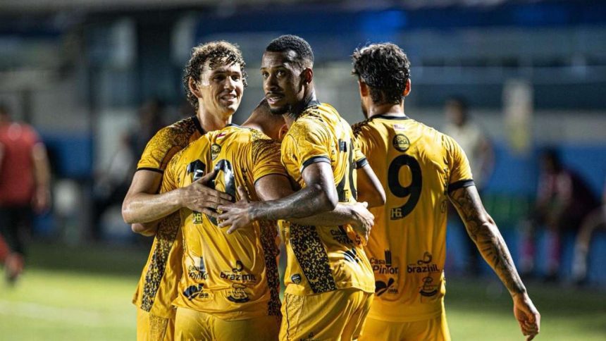 Jogadores do Amazonas FC celebrando um gol, abraçados e vestindo uniformes amarelos.