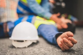 Acidente de trabalho: trabalhador ferido no chão, com capacete próximo e outros funcionários prestando socorro.