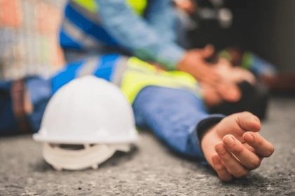 Acidente de trabalho: trabalhador ferido no chão, com capacete próximo e outros funcionários prestando socorro.