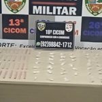 Apresentação de itens apreendidos pela polícia militar, incluindo uma placa de identificação e objetos sobre uma mesa.