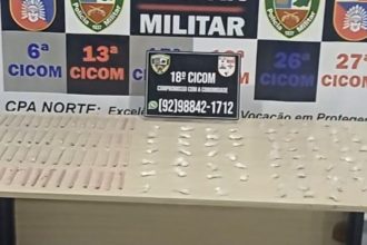 Apresentação de itens apreendidos pela polícia militar, incluindo uma placa de identificação e objetos sobre uma mesa.