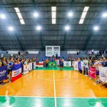 Cerimônia de abertura dos Jogos Universitários do Amazonas com bandeiras e equipes em quadra.