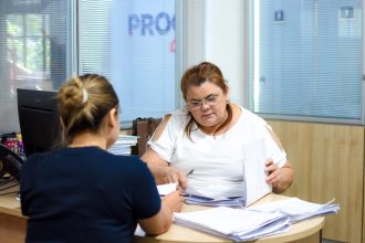 Duas mulheres em escritório oo Procon-AM analisando documentos. Uma delas usa óculos e veste branco.