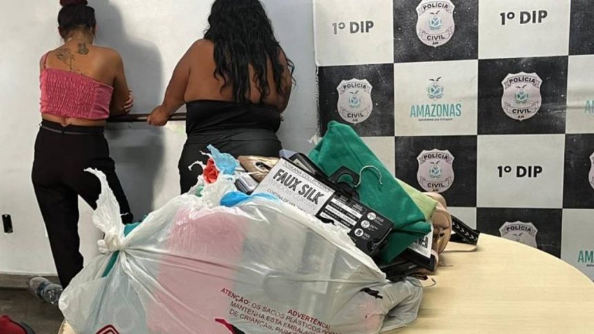 Duas mulheres em uma sala com evidências apreendidas, incluindo roupas e sacolas plásticas.