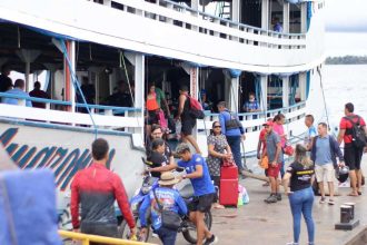 Pessoas embarcando e desembarcando de um barco em um píer, com um céu nublado ao fundo.