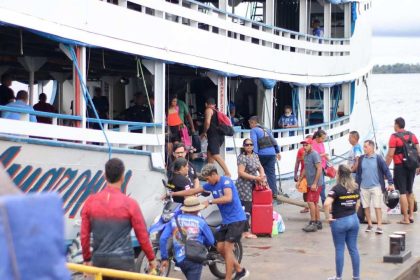Pessoas embarcando e desembarcando de um barco em um píer, com um céu nublado ao fundo.