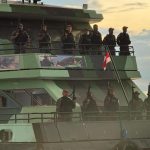 Policiais armados em barco, bandeira e pôr do sol ao fundo