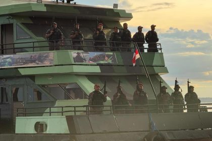 Policiais armados em barco, bandeira e pôr do sol ao fundo