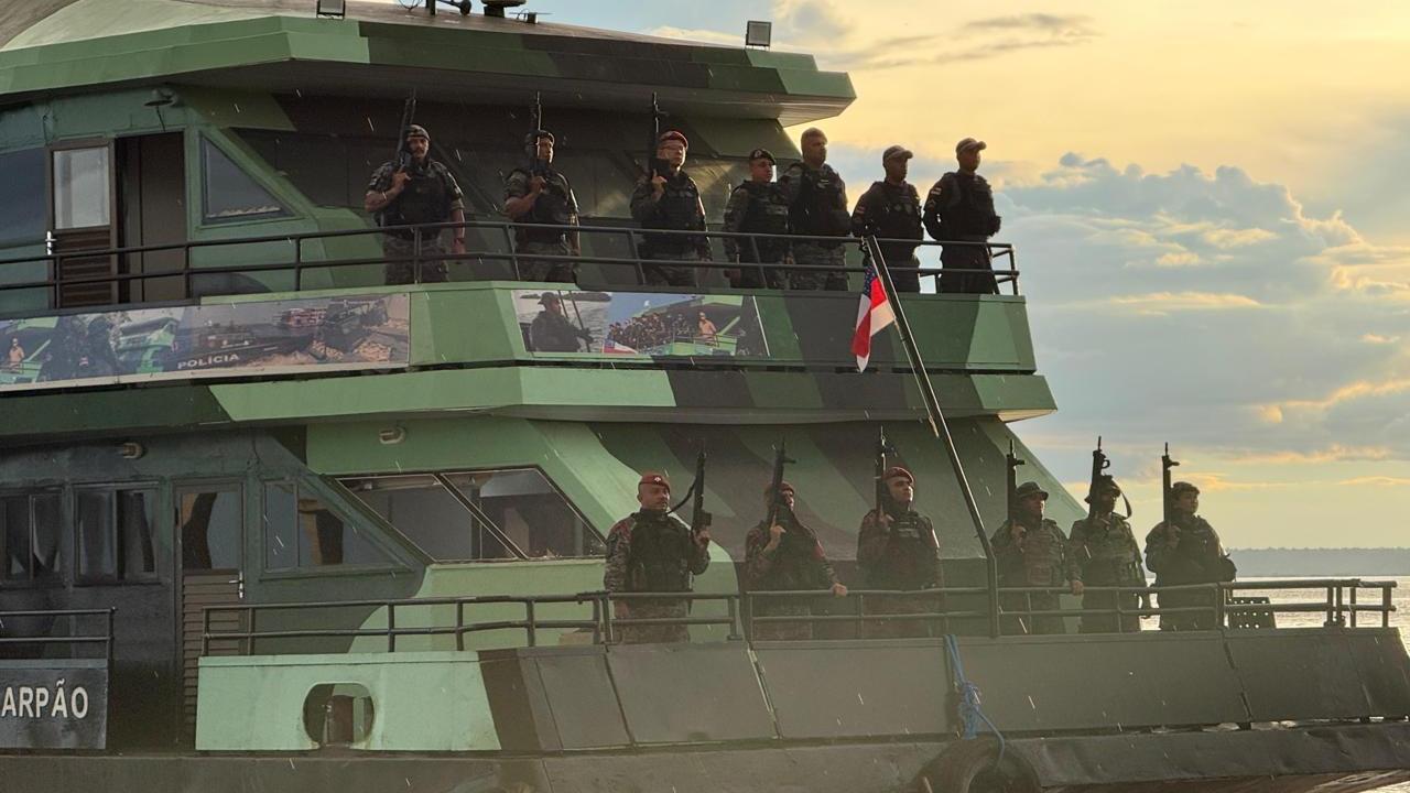 Policiais armados em barco, bandeira e pôr do sol ao fundo